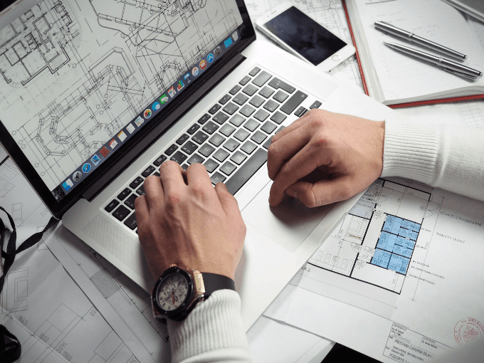 Person Working On Laptop With Blueprints Displayed On The Screen