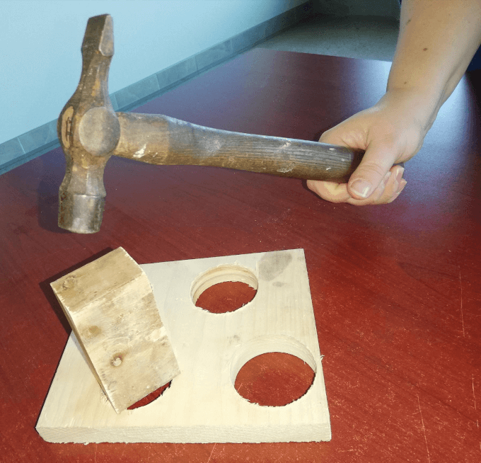 A Person Attempts To Force A Square Peg Into A Round Hole With A Hammer.